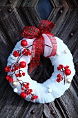Red berries and Christmas baubles on decorative wreath of white felt on rustic front door
