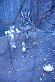 Glass candlesticks of various sizes and metal candelabra with crystal pendants on wooden deck next to lake