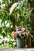 Summery bouquet in ornate zinc pot below white buddleia