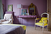 Bedroom with purple walls, gold-framed mirror and yellow accent chair
