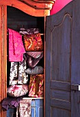 Patterned satin fabrics arranged in open, antique cupboard