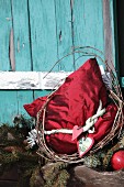 Red silk cushion with vintage Christmas decoration in front of turquoise cabin window shutter