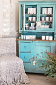 Packages of scented candles in turquoise dresser next to chair with loose cover