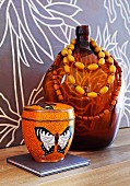 Tin painted with butterfly motif next to necklace of wooden beads hung on demijohn