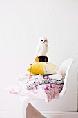 White owl ornament on stack of cushions on white plastic shell chair