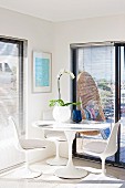 Orchid in spherical vase on Tulip table with matching white shell chairs in corner in front of balcony doors with louver blinds