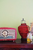 Fifties-style radio next to red paper lantern with black metal frame against pastel green wall