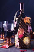 Wine bottle holder decorated with colourful, painted autumn leaves