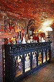 Console cabinet with backlit religious panels and hotchpotch of ornaments on top against brick wall
