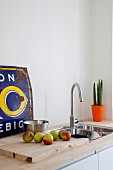 Apples on wooden chopping board in front of rusty advertising sign on simple sink unit with pale wooden worksurface