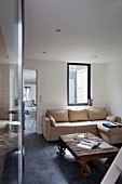 Blick durch geöffnete Tür auf rustikalen Couchtisch mit Rollen und helles Sofa in Zimmerecke vor Fenster