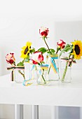 Single sunflowers and roses in glass vases decorated with ribbon