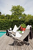 Butterfly chairs with white seats on wooden deck at edge of pool