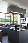 Essensvorbereitung auf Mittelblock mit grauen Unterschränken gegenüber Küchenzeile an Sprossenfenster mit Gartenblick