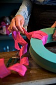 Hands of woman creating wreath of flowers using oasis foam and deep pink silk ribbon