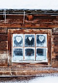Aufgehängte Herzformen im Fenster eines Blockhauses in winterlicher Stimmung