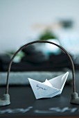 Paper boat with name seen through stylised bridge on dark table top