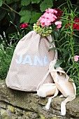 Hand-sewn, polka dot sports bag with sewn-on name next to ballet shoes on stone wall in garden