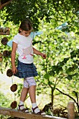 Kind mit selbsgenähtem Shirt beim Balancieren auf Holzbalken im Garten