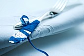 Fork wrapped in blue ribbon on linen napkin