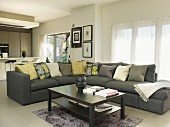 Coffee table in front of corner sofa with scatter cushions in open-plan interior