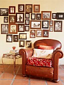 Alter brauner Ledersessel und Beistelltisch vor Wand mit gerahmter Fotosammlung