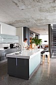 Blick von Designerküche mit Küchenblock in offenen Wohnbereich mit Treppe, polierter Betonboden und rohe Betondecke