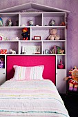 Toys arranged on white shelving with triangular roof built around girl's bed with pink upholstered headboard