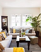 Comfortable sofas with many scatter cushions, corner cabinet with glass door and black and white striped rug in front of open lattice windows