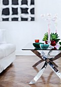 Heavy bowls and candelabra in coloured glass on retro designer table; modern artwork on wall in blurred background