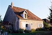 Old, French farm house with white window shutters in simple, one-storey stone facade