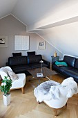 Attic living room with fur blanket on white armchair and black leather sofa set around DIY coffee table