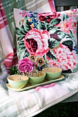Gypsophila in green bowls and rose on tray in front of cushion with rose motif on checked blanket