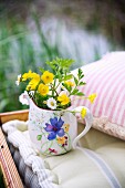 Small painted jug of wild flowers on seat cushion next to pink and white striped scatter cushion