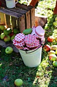 Vintage wooden crate of harvested apples and preserving jars with red and white fabric covers in enamel bucket