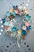 Artistic wreath of small, pastel origami flowers hung on grey metal panel with perforated pattern