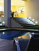Pool in front of illuminated steps leading to dining area on platform in yellow-painted interior