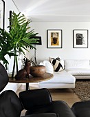 Foliage and rabbit ornament on round wooden side table, modern, white corner sofa and framed pictures in background