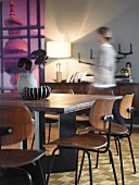 Classic wooden chairs at modern dining table; woman in background in front of lit table lamp on sideboard