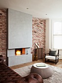 Coffee table in front of open fireplace in concrete chimney breast flanked by brick walls and armchair in corner