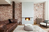 Lounge area with old leather sofa and coffee table on rug in front of modern fireplace in brick wall in open-plan interior