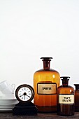 White china, table clock and old apothecary bottles against white wall