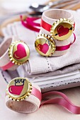 Gold bottle cap and heart motif and pink ribbons on wooden napkin rings