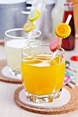 Glasses of orange and lemon drinks with straws decorated with the appropriate fruit motifs on bottle tops