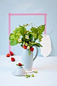 Pale blue jug of fresh strawberries, strawberry flowers and lady's mantle