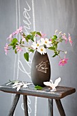 Cosmea in dark grey retro vase on old wooden stool in front of grey wall