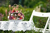 Romantische Gebäck-Etagere mit Rosen und anderen Blüten geschmückt auf weißer Lochstickerei-Tischdecke im sommerlichen Garten
