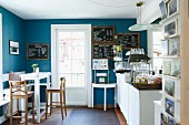 Nostalgic sales room with bistro stools, white counter table and blackboards on blue walls; country-house ambiance