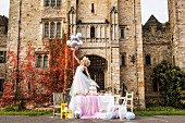 Bride holding balloons standing on festively set table in front of manor house