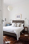 Blick ins Schlafzimmer auf Doppelbett mit gepolstertem Kopfteil und silbergrauen Dekokissen
